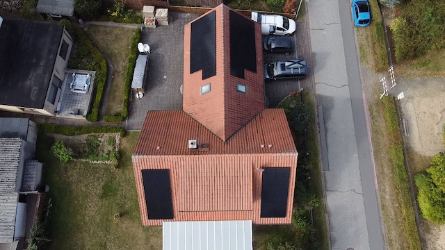 Luftbild eines EFH mit PV-Anlage Dach eines Hauses mit roten Ziegeln und Solarpanelen, umgeben von Grünflächen.