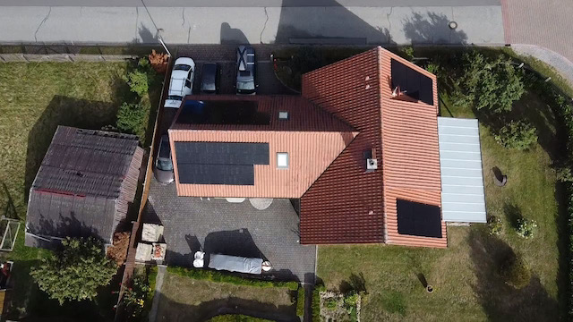 PV-Anlage aus der Luft Dachansicht eines Hauses mit Solarzellen und mehreren Fahrzeugen im Hof.